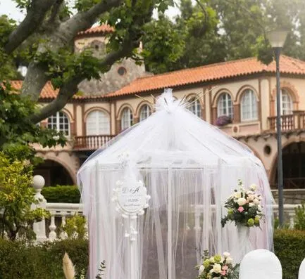 Hermosa configuración de boda al aire libre con cortinas blancas y arreglos florales bajo un árbol.