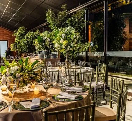 Evento interior estiloso con mesas redondas decoradas con centros de mesa florales y vajilla elegante.