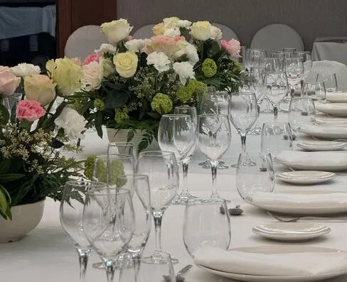 Una mesa de comedor bellamente dispuesta con cristalería y centros de mesa florales en un entorno elegante.