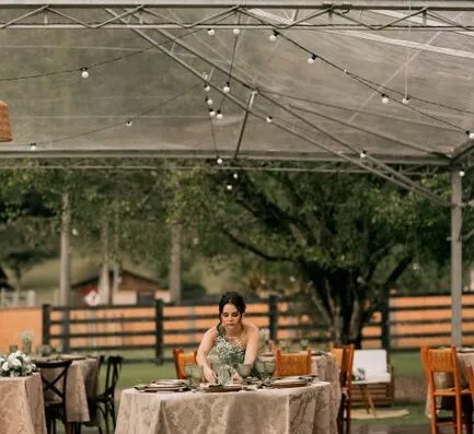 Elegante decoración para una recepción de boda al aire libre, con una mujer arreglando la decoración de las mesas bajo un toldo.