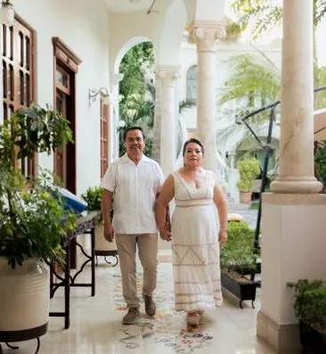 Pareja de la mano mientras caminan por una elegante columnata de hotel, rodeados de exuberante vegetación.