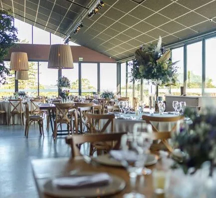 Salón de recepción de bodas elegante con decoración de alta gama, luz natural y mesas elegantemente dispuestas.