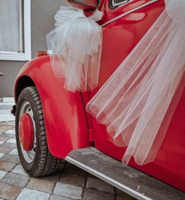 Primer plano de un coche clásico rojo con decoraciones de tul blanco para un evento de boda.