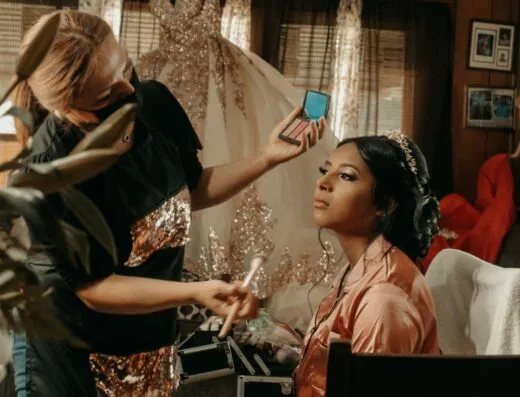 Un maquillador aplica cosméticos a una novia durante los preparativos de la boda en interiores.