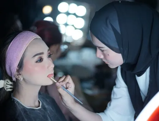 Una maquilladora aplicando lápiz labial a un modelo en un estudio de belleza.