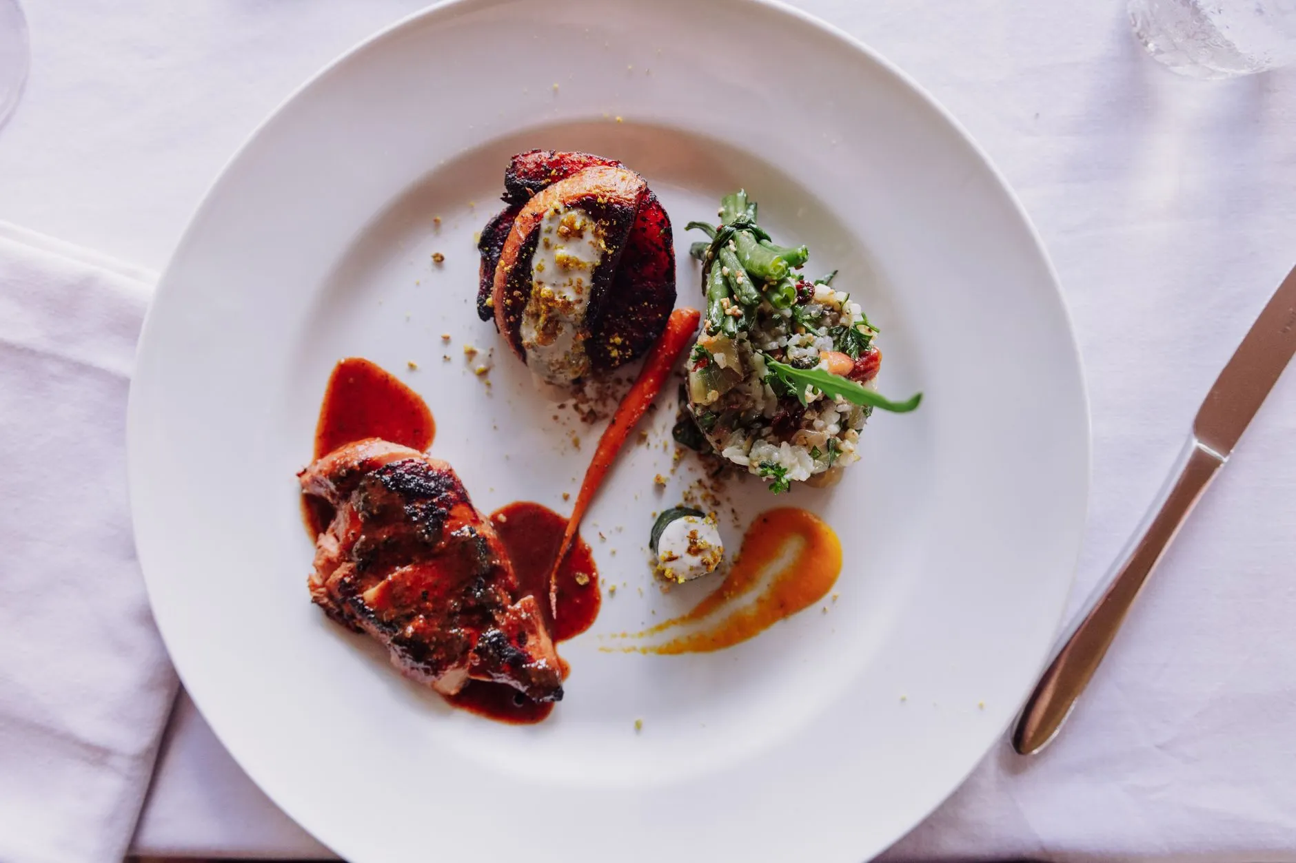 Elegante plato gourmet con carne a la parrilla y arreglo artístico de vegetales.