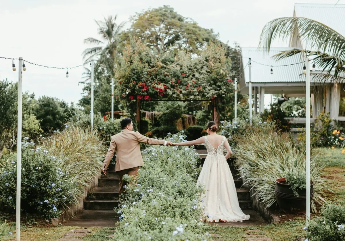 Una pareja de recién casados de la mano en un jardín frondoso, capturada desde atrás (imagen de referencia)