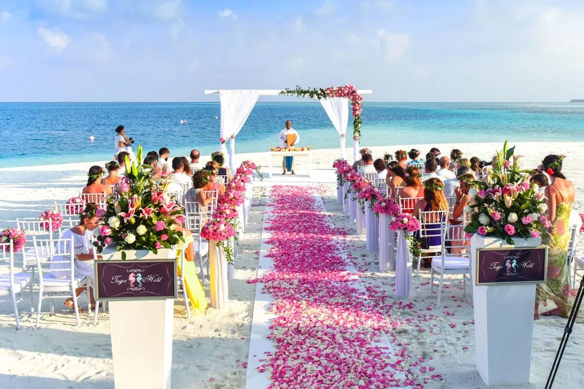 Una hermosa decoración de boda en la playa al aire libre con pétalos de rosa, invitados y vista al océano (imagen de referencia)