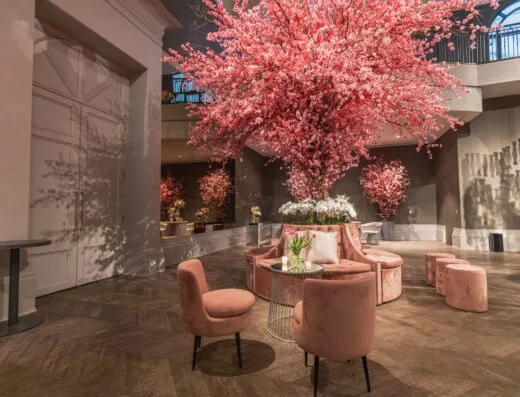 Lobby de hotel de lujo adornado con flores de cerezo rosas y un elegante arreglo de asientos.