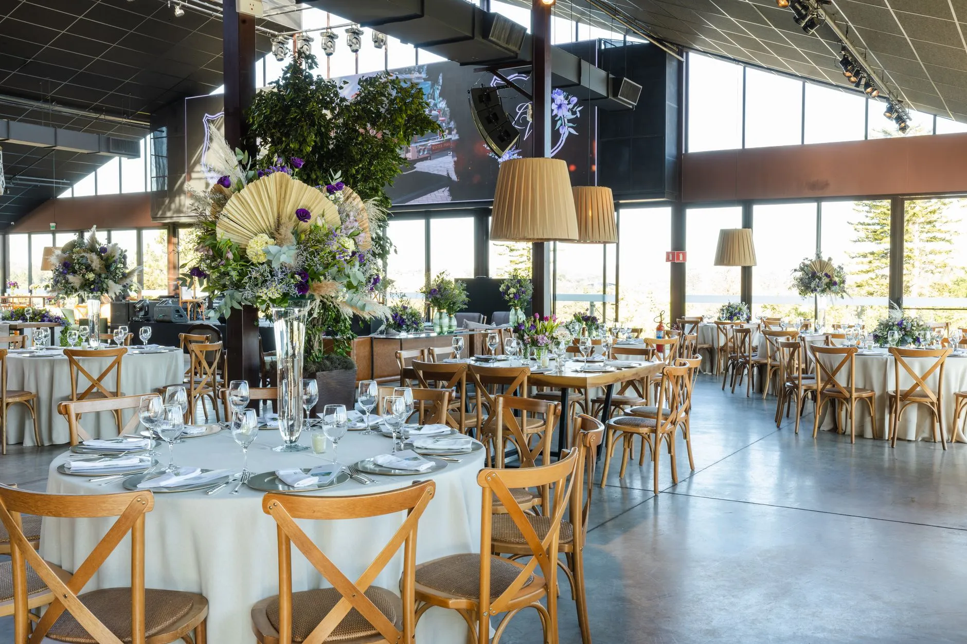 Un salón de recepción de bodas bellamente decorado con arreglos florales, iluminación elegante y mesas organizadas.