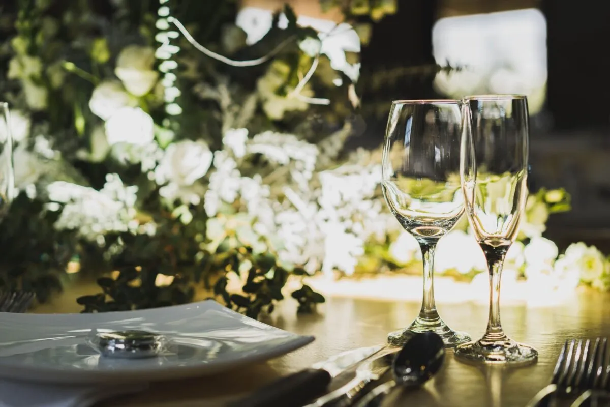 Un elegante primer plano de la decoración de mesa de boda con copas, cubiertos y arreglo floral (imagen de referencia)