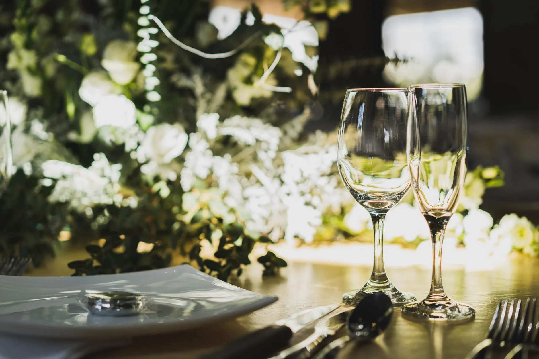 Un elegante primer plano de la decoración de mesa de boda con copas, cubiertos y arreglo floral (imagen de referencia)