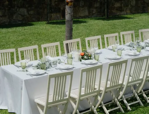 Mesa de boda elegante al aire libre con sillas blancas y decoración floral en un día soleado de verano.