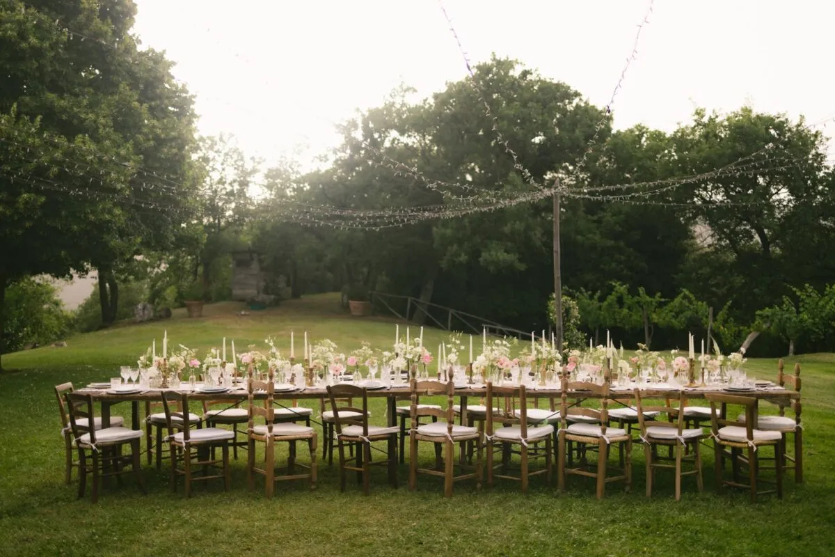 Hermosa mesa de recepción de boda al aire libre con decoraciones florales y luces colgantes en un jardín (imagen de referencia)