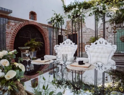 Configuración de boda lujosa al aire libre con sillas elegantes, decoraciones florales y mesa espejo.