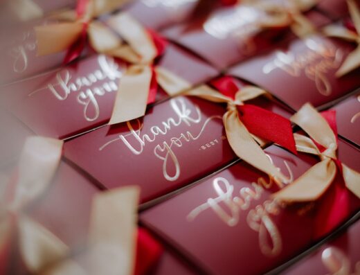 Un primer plano de cajas de regalo rojas bellamente envueltas con etiquetas de "Gracias" y cintas doradas.