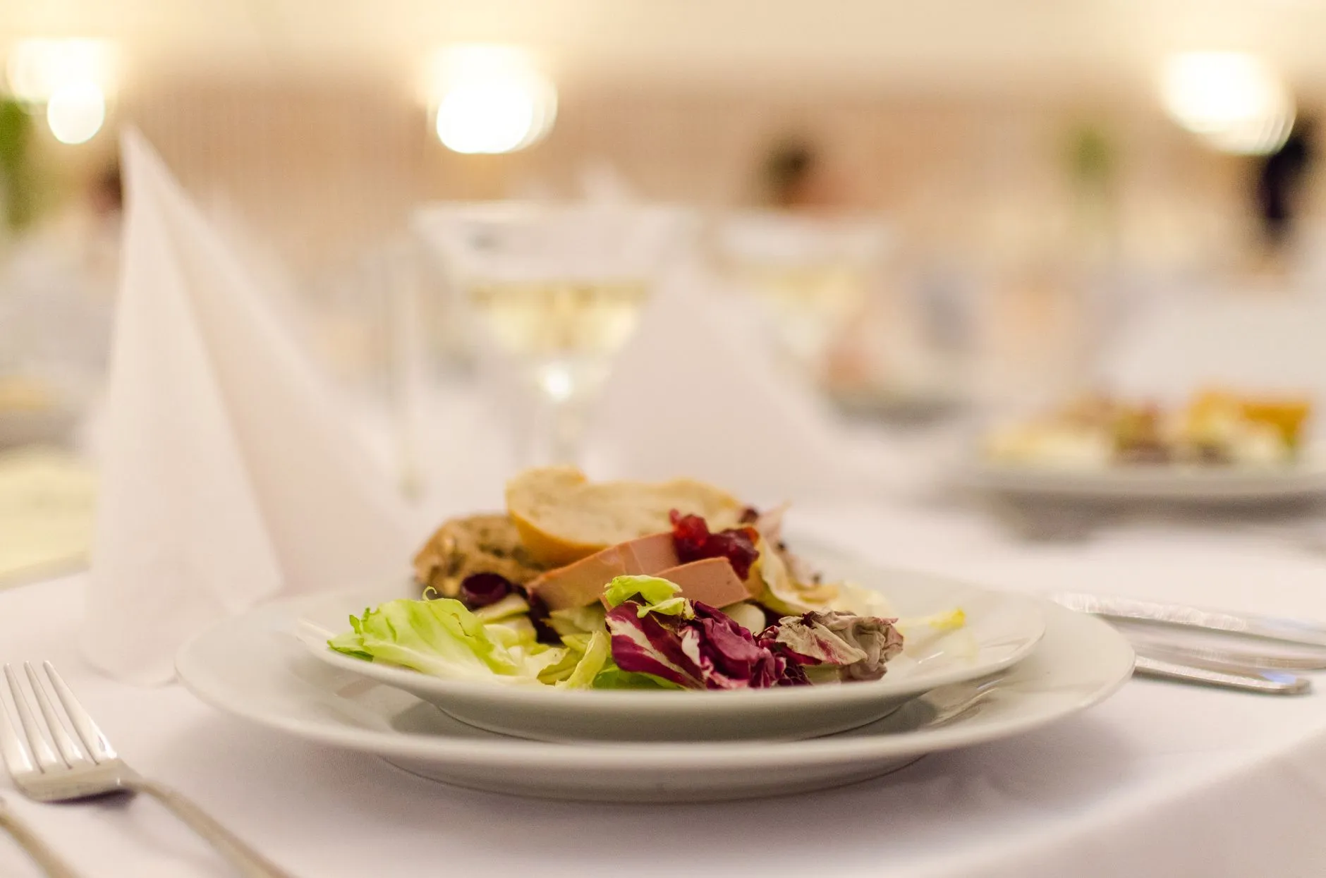 Plato de ensalada gourmet con pan en una mesa de restaurante elegantemente dispuesta, perfecta para experiencias de alta cocina.