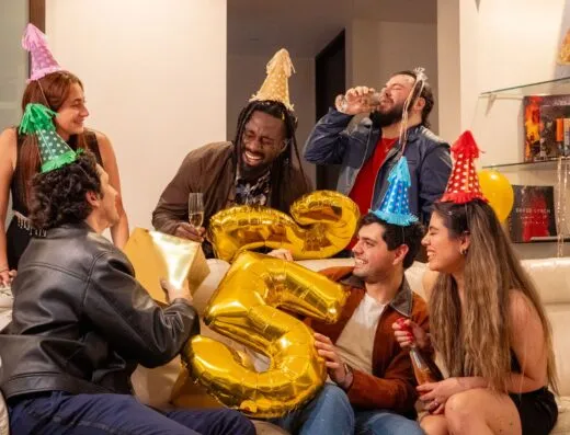 Grupo feliz de amigos celebrando un cumpleaños con globos y gorros de fiesta.