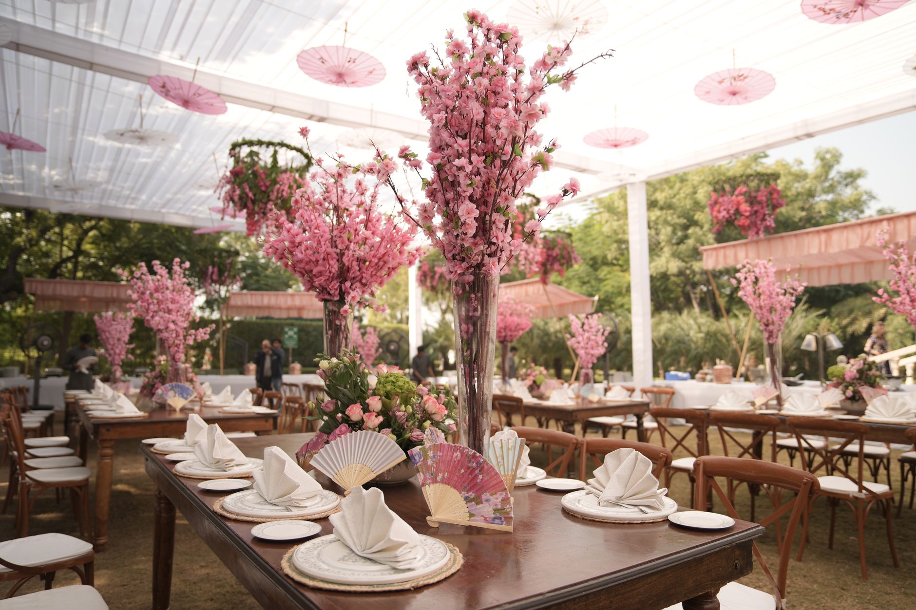 Impresionante configuración de boda india al aire libre con decoración floral rosa y abanicos tradicionales.