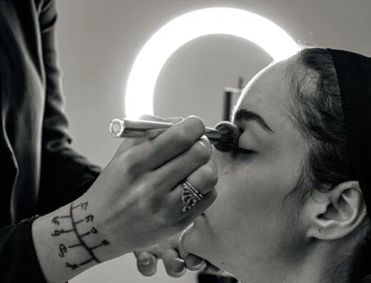 Una maquilladora aplica maquillaje profesional a una mujer con un pincel en un estudio.