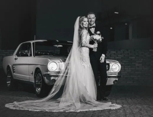 Una fotografía en blanco y negro de una pareja feliz el día de su boda, posando con un automóvil clásico en Asunción, Paraguay.