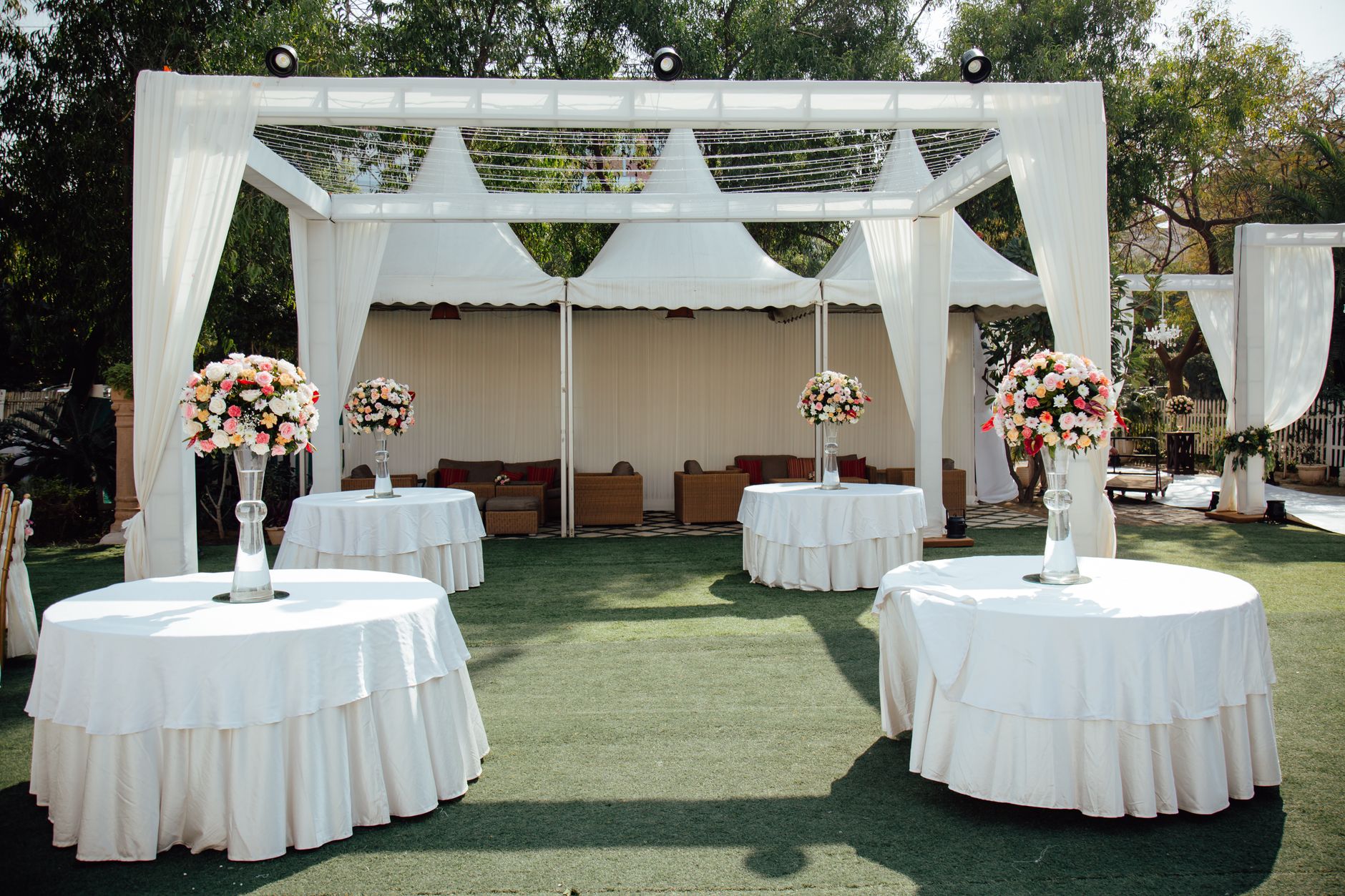 Encantador arreglo de boda al aire libre con pérgolas cubiertas de blanco y centros de mesa florales bajo un cielo soleado.