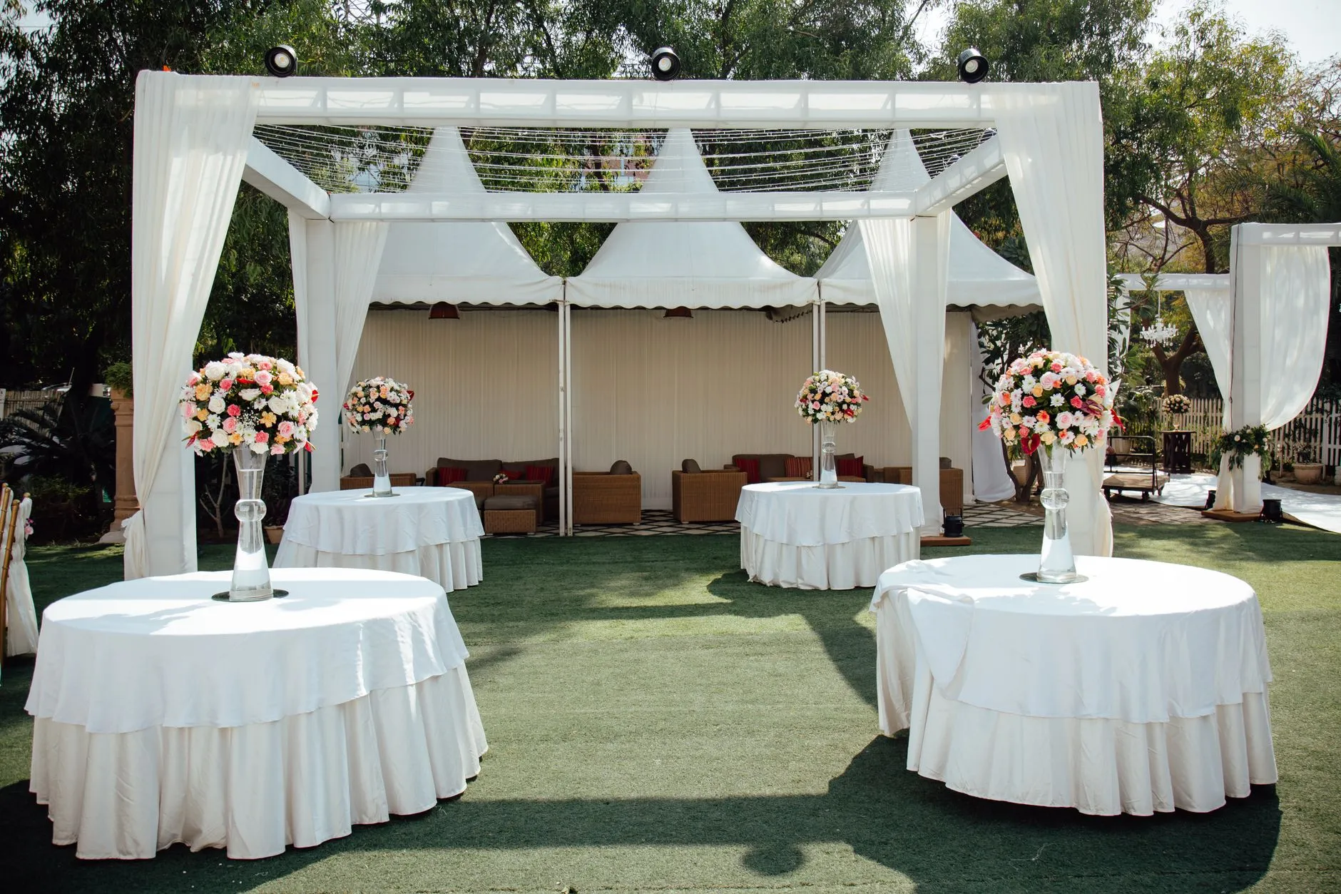 Encantador arreglo de boda al aire libre con pérgolas cubiertas de blanco y centros de mesa florales bajo un cielo soleado.