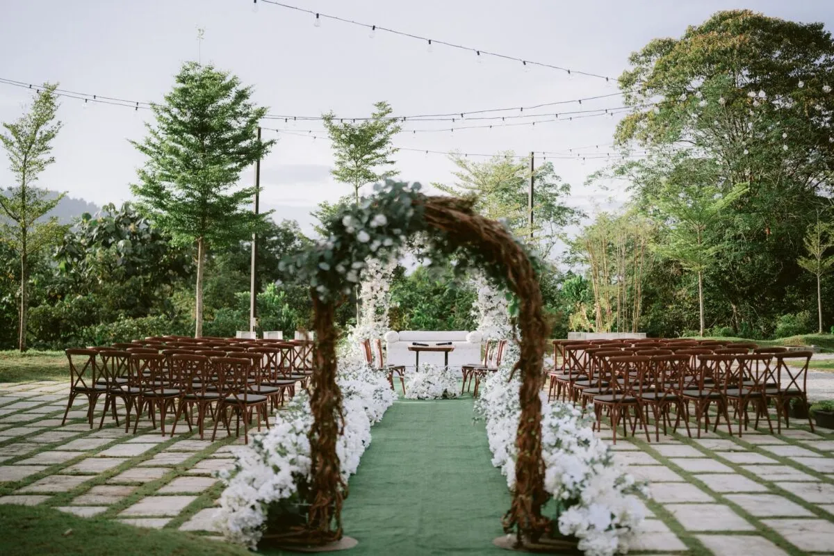 Hermoso montaje de ceremonia de boda al aire libre con arco, sillas y luces en un jardín exuberante (imagen de referencia)