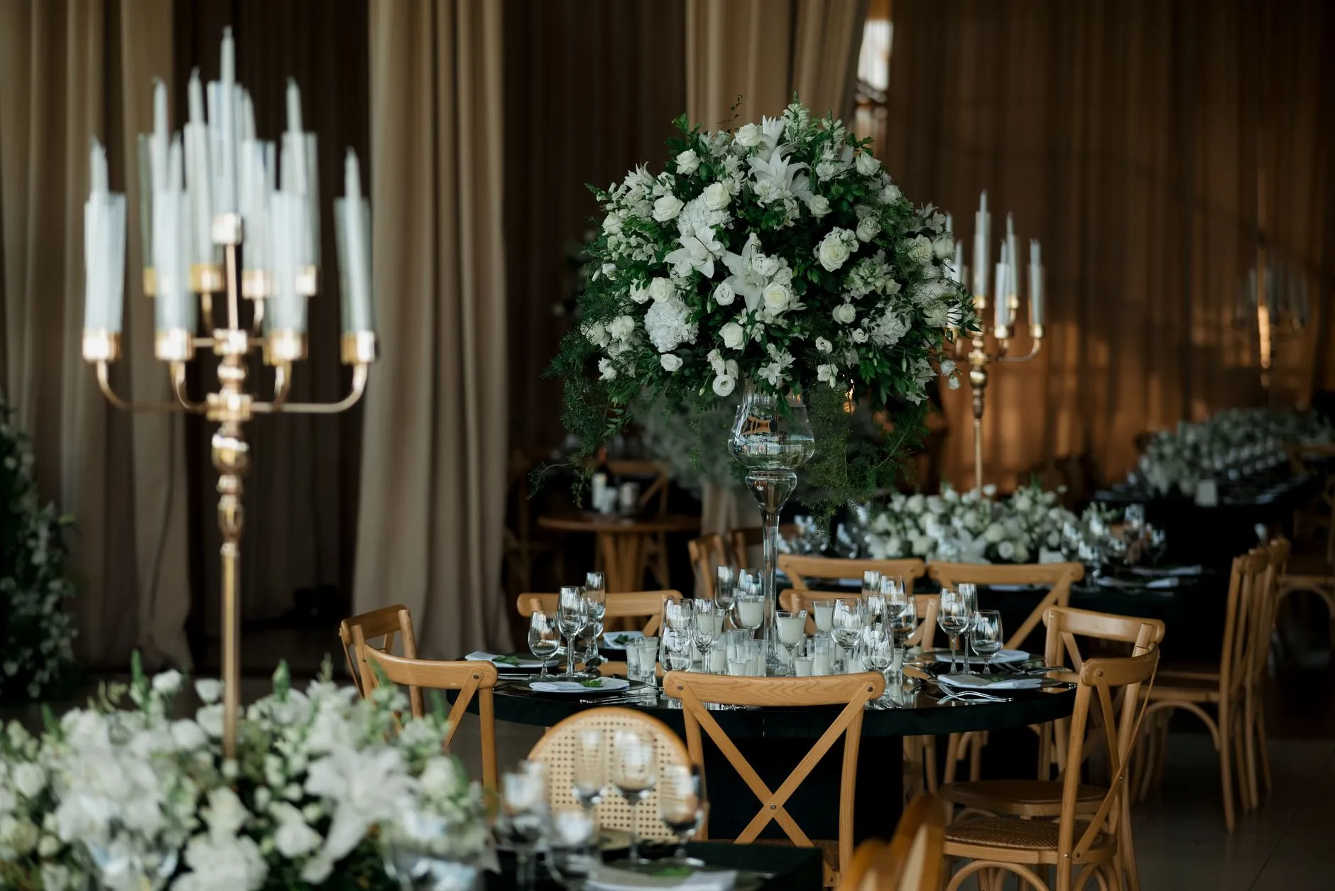 Configuración de recepción de boda de lujo con elegantes arreglos florales y mesas iluminadas con velas en un sofisticado lugar interior.