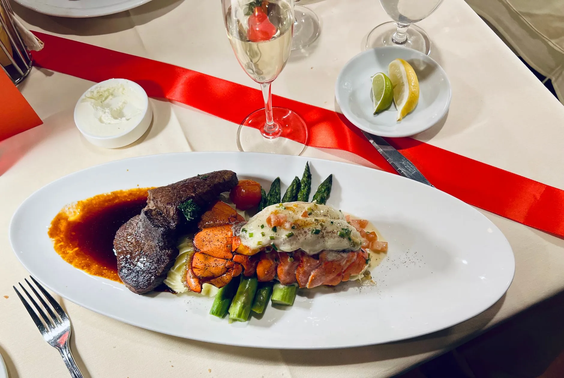 Elegante cena de surf and turf con filete, langosta y espárragos, acompañada de champán.