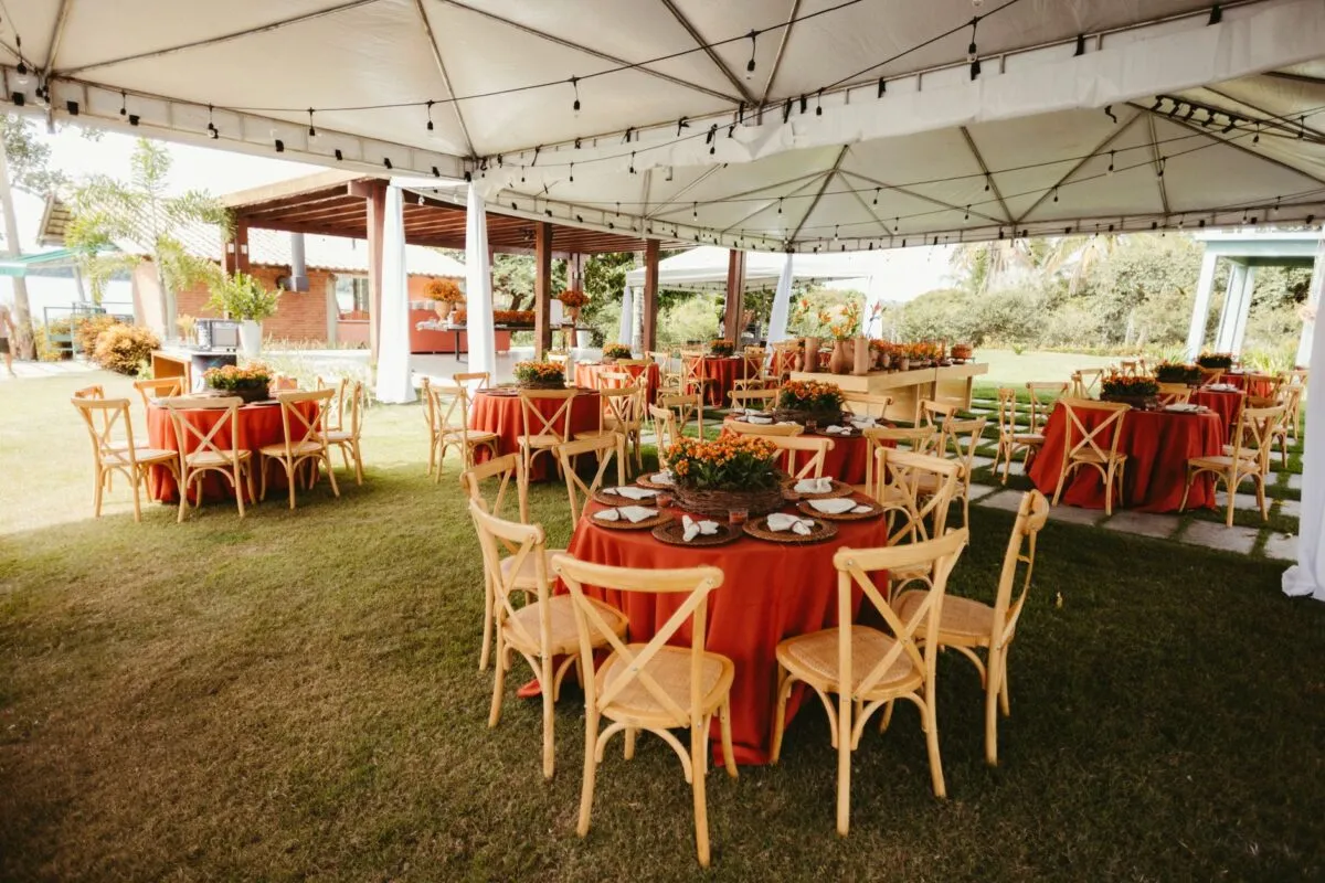 Preciosa recepción de boda al aire libre con mesas decoradas en rojo y sillas de madera bajo una carpa (imagen de referencia)