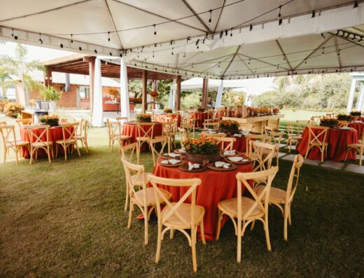 Preciosa recepción de boda al aire libre con mesas decoradas en rojo y sillas de madera bajo una carpa.