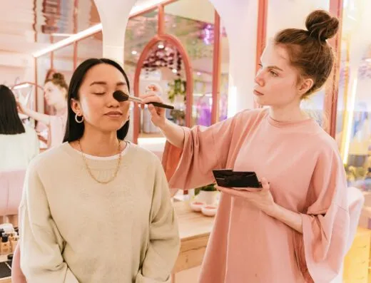 Mujer asiática recibiendo maquillaje de un artista en un salón de belleza moderno y luminoso.