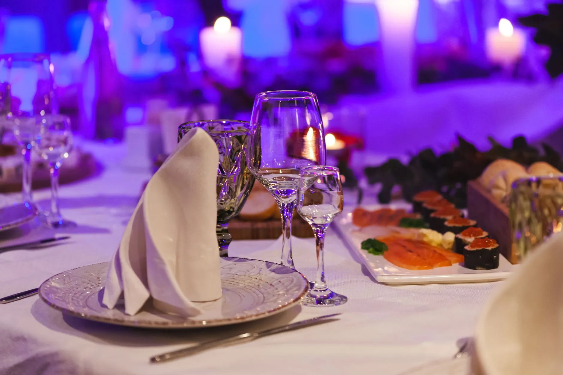 Arreglo de mesa sofisticado con plato de sushi, velas y elegantes cristalerías, perfecto para un ambiente de cena elegante.