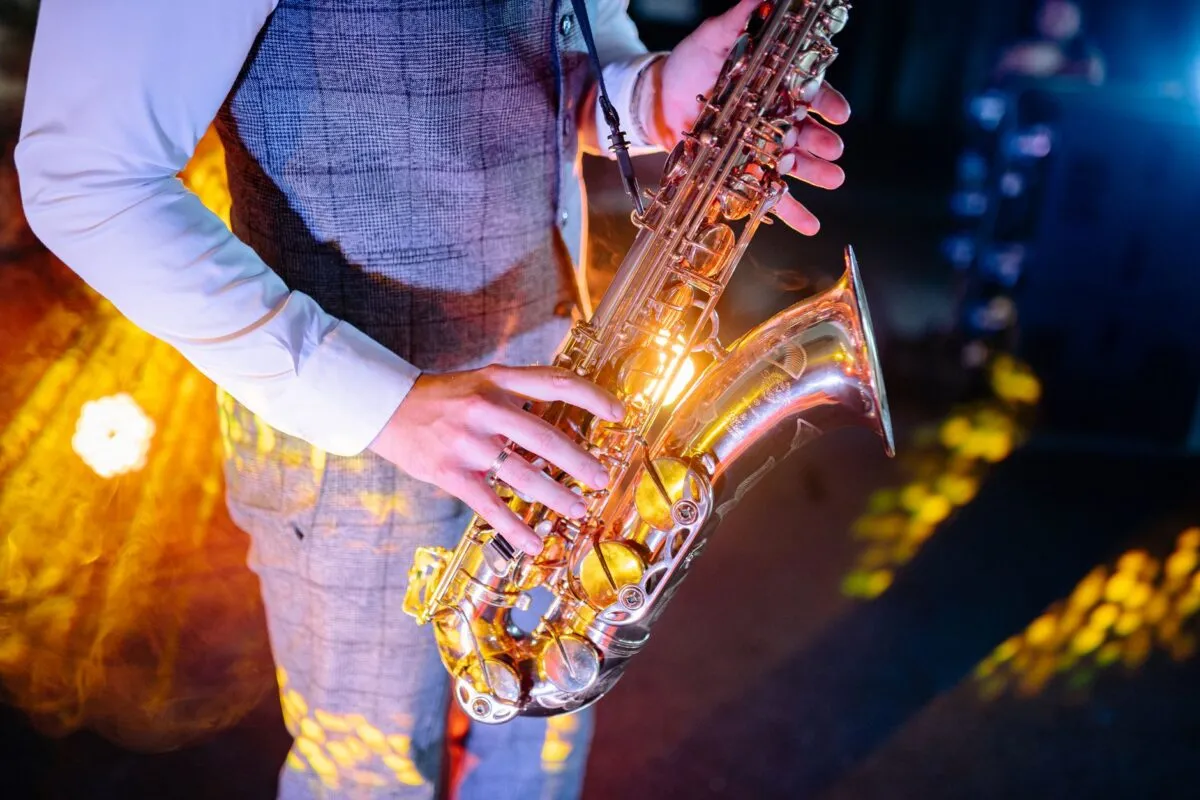 Primer plano de las manos de un músico tocando el saxofón bajo luces de escenario coloridas (imagen de referencia)