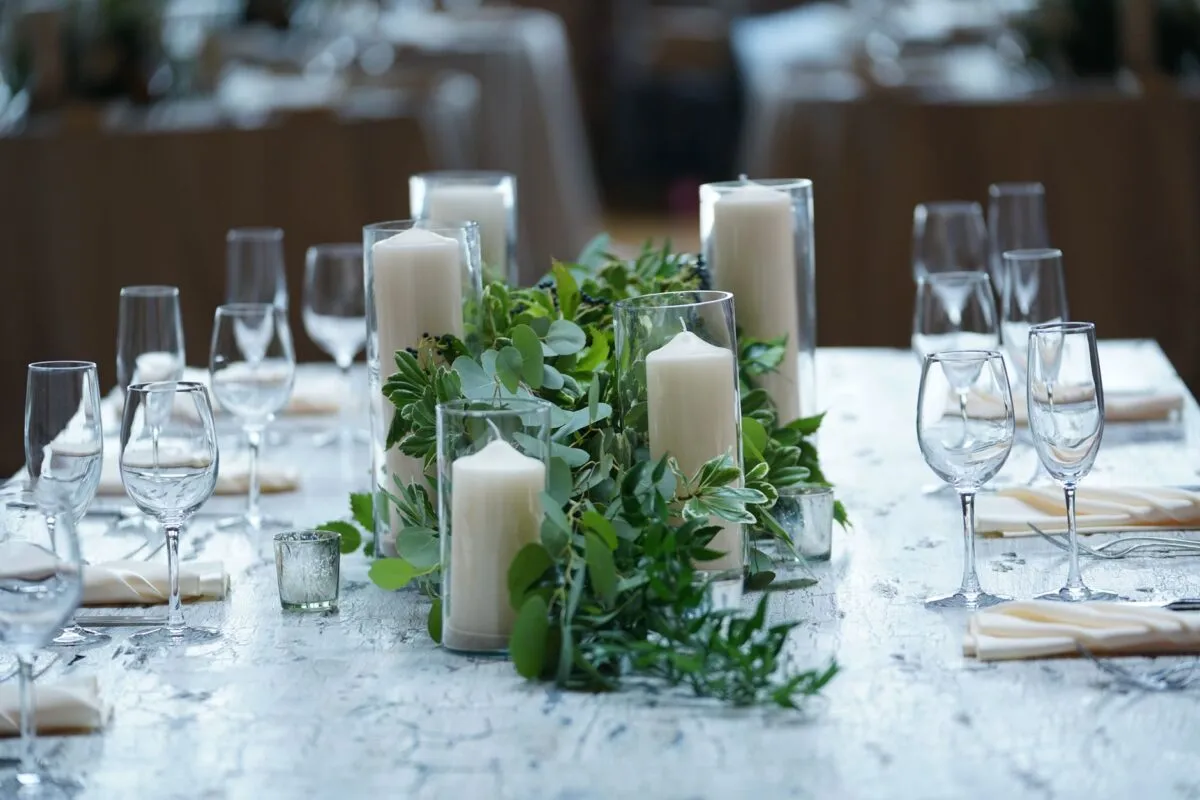 Hermoso montaje de mesa de boda con velas blancas, cristalería y exuberante vegetación en un entorno elegante (imagen de referencia)