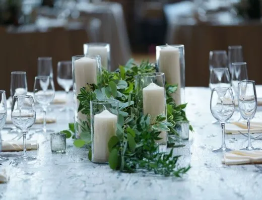 Hermoso montaje de mesa de boda con velas blancas, cristalería y exuberante vegetación en un entorno elegante.