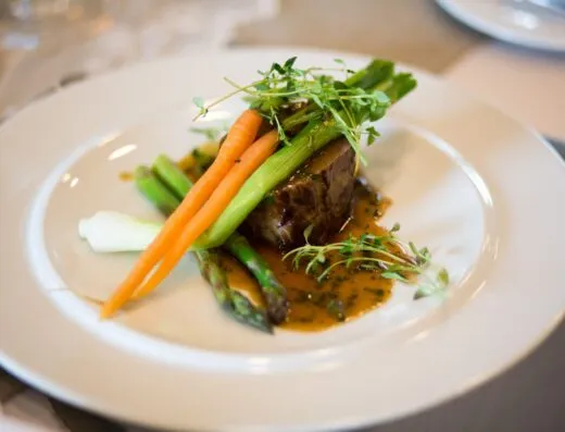Comida gourmet lujosa elegantemente presentada con verduras y salsa.