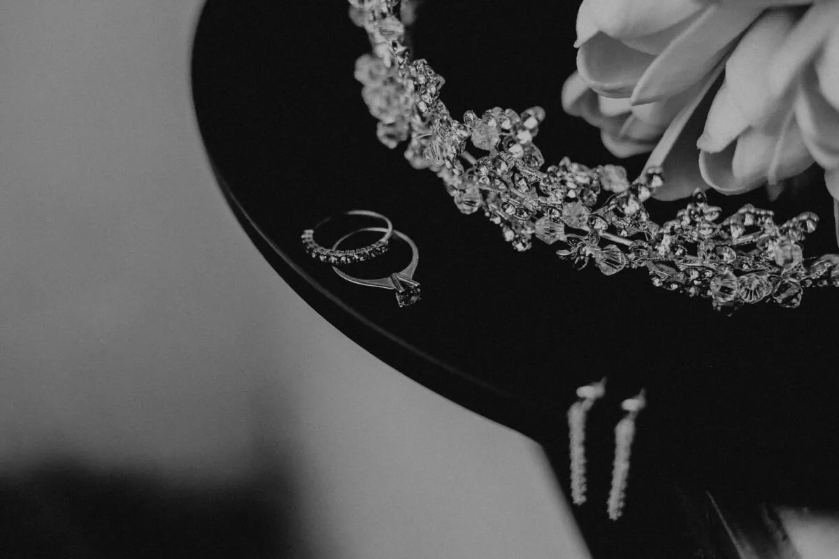 Primer plano de joyería de boda elegante en blanco y negro, que presenta anillos y una tiara (imagen de referencia)