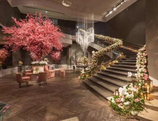 Un gran vestíbulo de hotel con exquisitas decoraciones florales, escalera de caracol y elegantes candelabros.