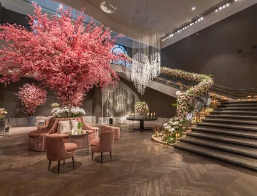 Lobby de hotel lujoso con grandes arreglos florales y escalera elegante.