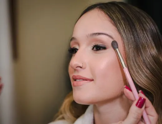 Primer plano de una mujer joven aplicando maquillaje con un pincel, mostrando belleza y elegancia.