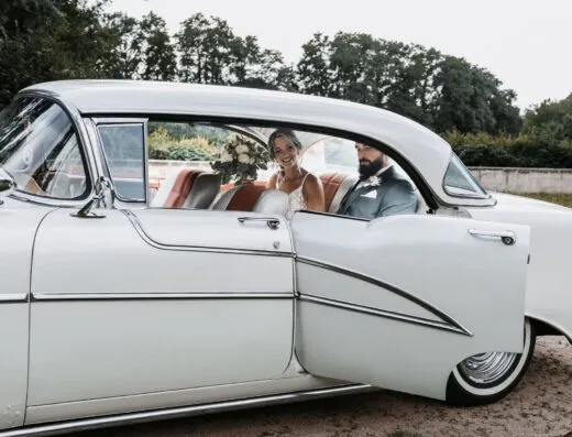 Pareja de novios en un coche blanco clásico, sonrientes y alegres en su día especial.