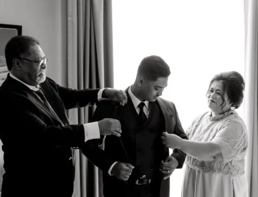 Una fotografía en blanco y negro que captura a un novio asistido por su familia antes de la ceremonia de la boda.