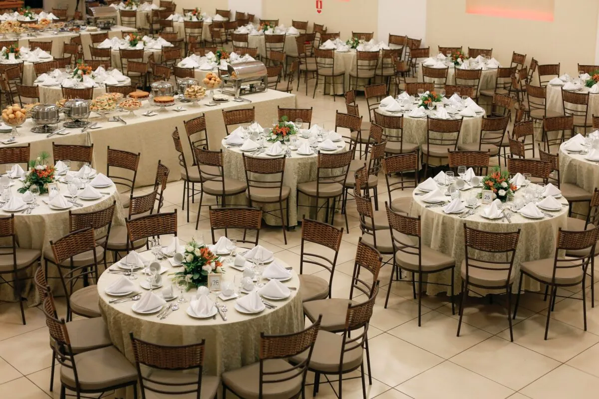 Amplia configuración de banquete con mesas redondas ordenadamente dispuestas y centros de mesa florales, lista para un gran evento (imagen de referencia)