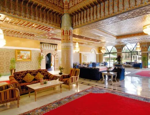 Lobby de hotel marroquí sofisticado con decoración ornamentada, asientos acolchados y candelabros.