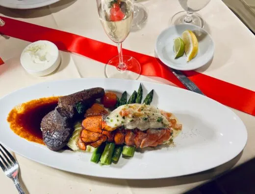 Elegante cena de surf and turf con filete, langosta y espárragos, acompañada de champán.