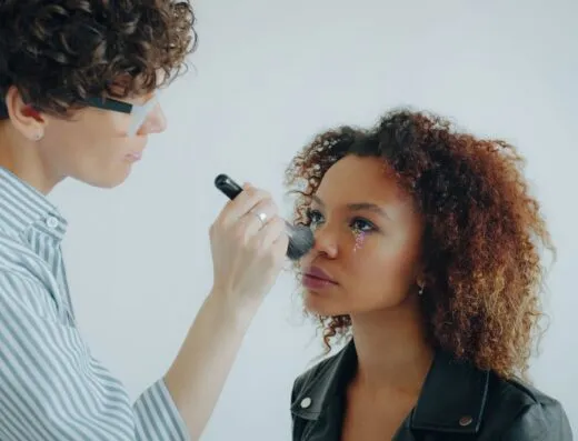 Una maquilladora aplica delicadamente colorete a una modelo con un maquillaje de ojos floral.