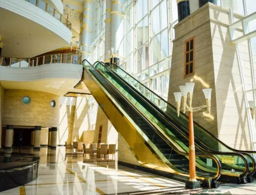 Una escalera mecánica de vidrio moderna en un espacioso atrio con luz natural brillante.
