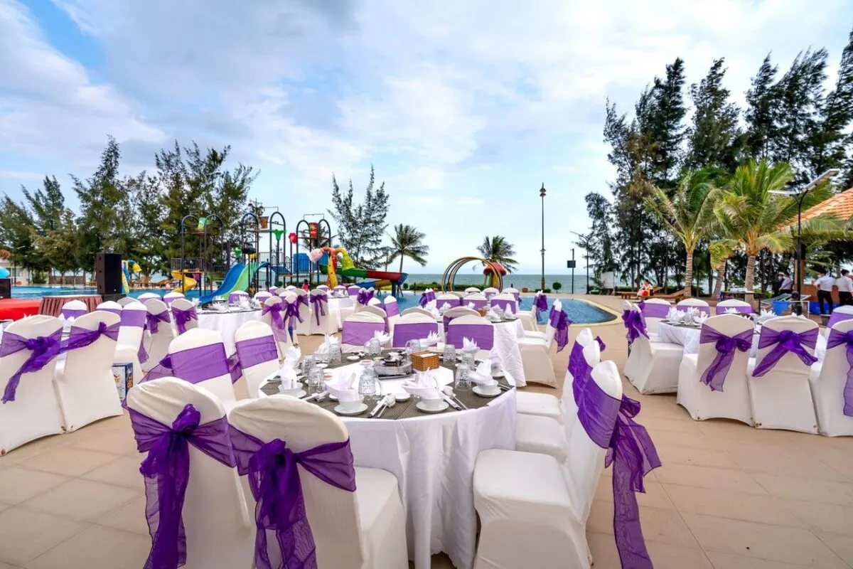 Hermoso entorno de boda al aire libre con acentos morados junto al mar, con sillas y mesas blancas (imagen de referencia)